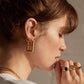 Side profile, model -brown hair up in bun, wearing Pawnshop Gold Plated Sterling Silver Large & Small Rectangle Hoop Earrings, Two tone hoop earrings. Models hand to mouth, wearing a select of Vintage Pawnshop 9K Gold Rings.