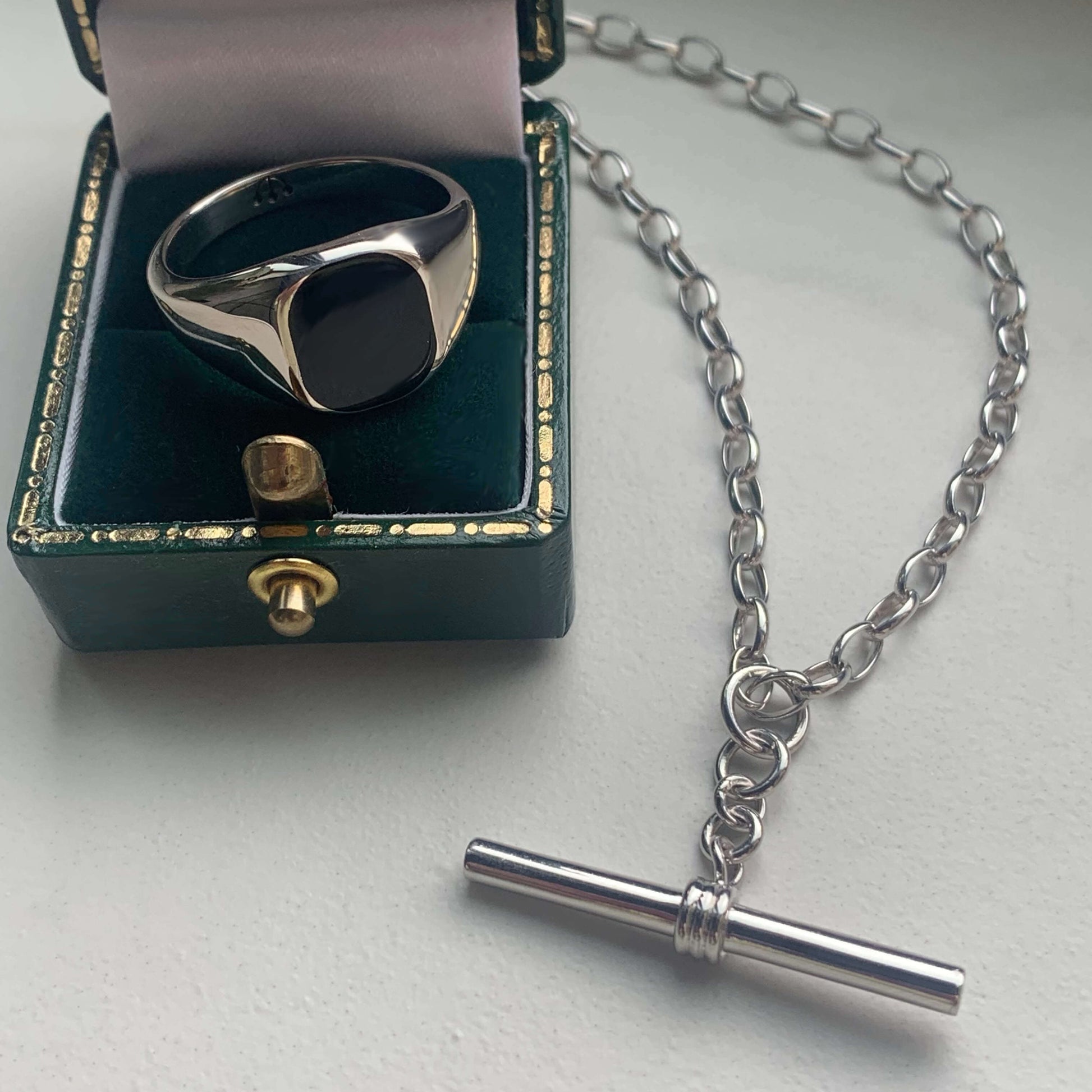 SILVER & BLACK ONYX CUSHION SIGNET RING IN DARK GREEN JEWELLERY BOX, STYLED NEXT TO SILVER T BAR CHAIN NECKLACE.