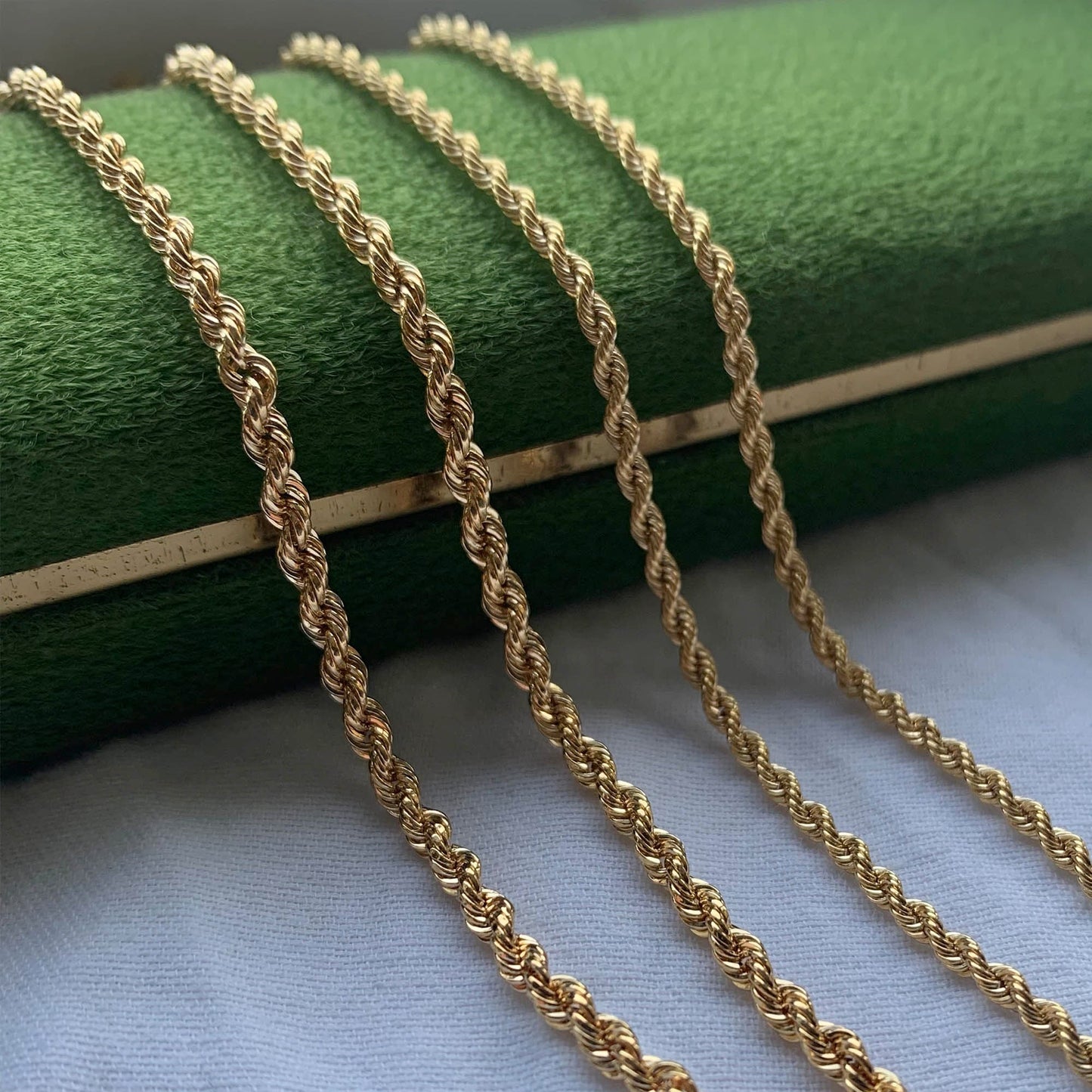 FOUR STRANDS OF ROPE CHAIN STYLED OVER A DARK GREEN JEWELLERY BOX.