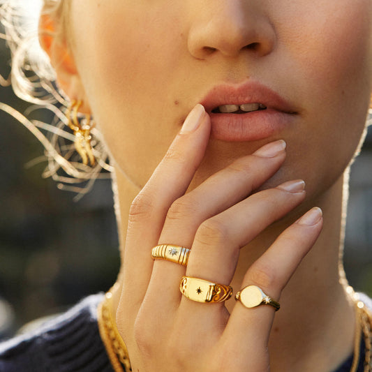 CLOSE UP MODEL WITH HAND TO FACE WEARTING PAWNSHOP SIGNATURE RIBBED STARBURST BAND, FILIGREE STARBURST AND PINKY STARBURST RINGS- ALL IN GOLD PLATED.