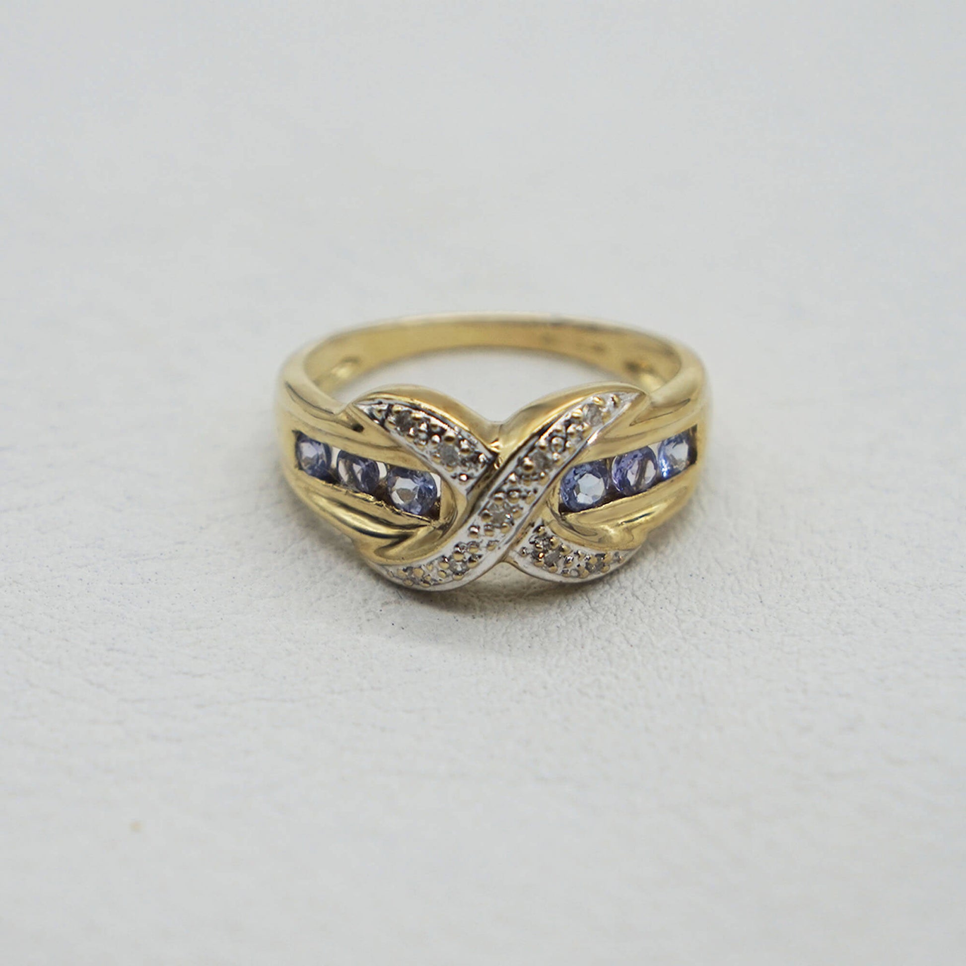 Vintage 9K gold diamond kiss setting- tanzanite stones set across band on white textured background.