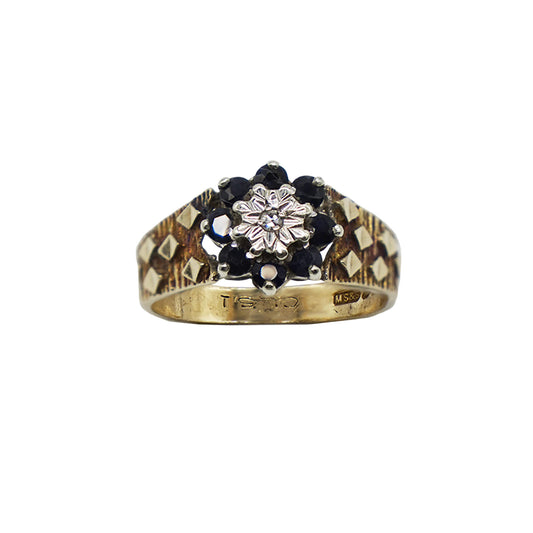 vintage 9k gold wide band ring with textured diamond shape detail on band and a centre flower of sapphire and diamond. Hallmarks visible on inner band.